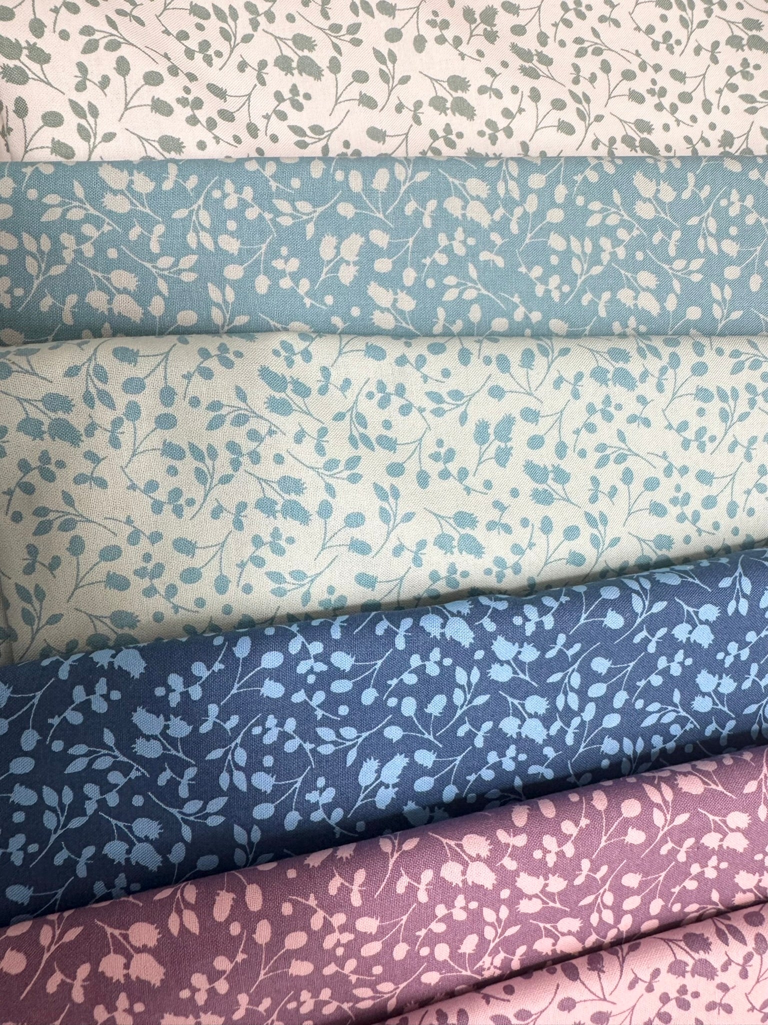 Stack of fabric fat quarter bundle with floral patterns in blue, purple, and white. For quilting.