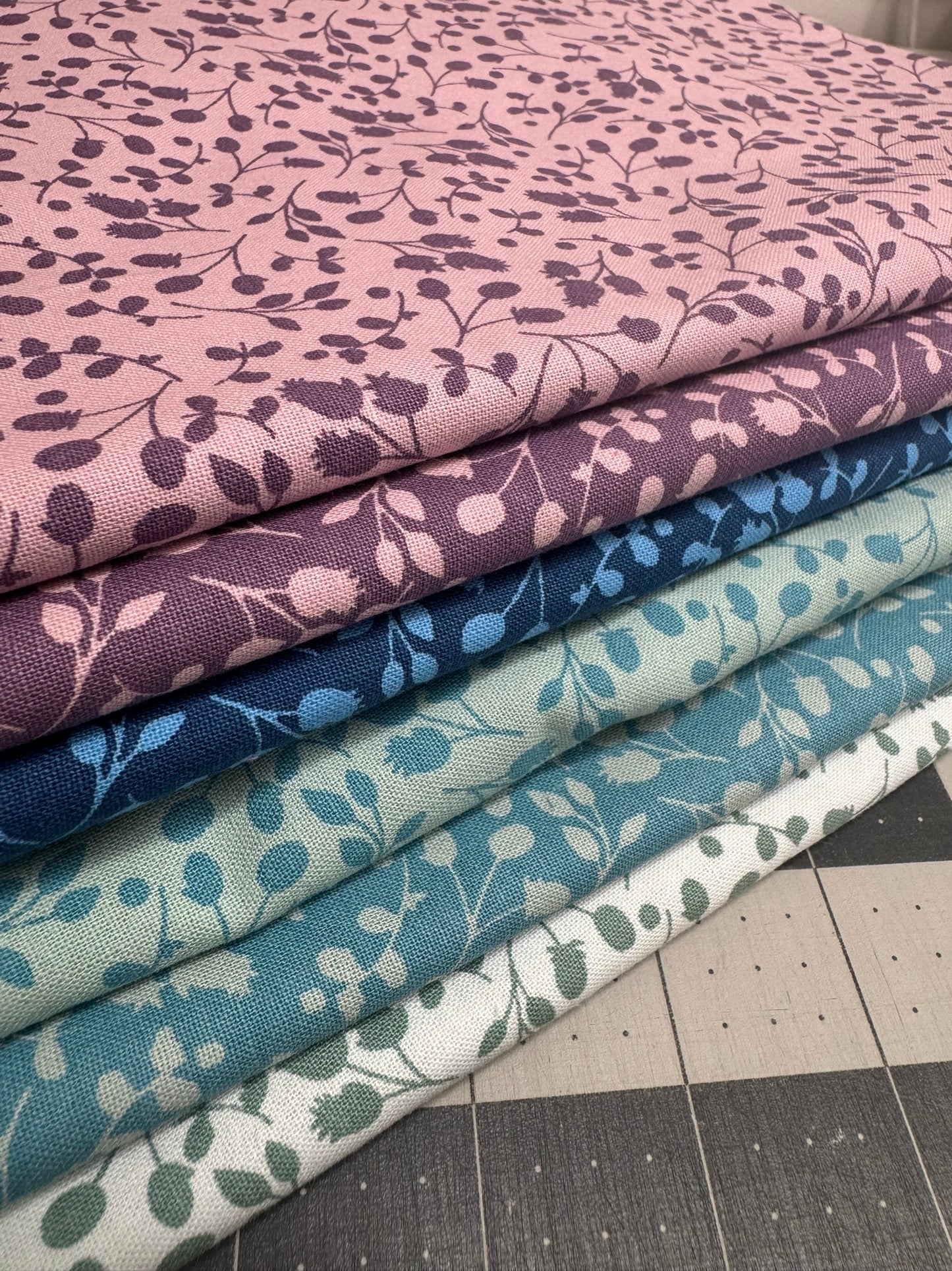 Stack of fabric swatches with floral patterns in various colours for quilting.
